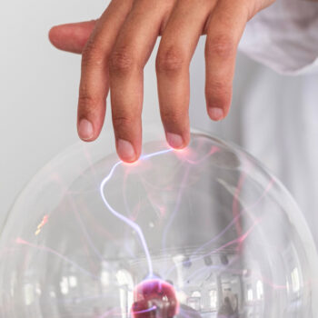 Finger berührt eine leuchtende Plasmakugel, aus der violette und rote elektrische Entladungen strahlen.