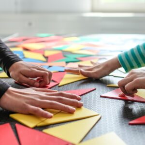 Hände legen bunte Dreiecke aus Pappe auf eine schwarze Unterlage mit Rastermuster.