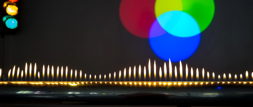 Brennende Kerzen in einer Reihe vor unscharfen roten, grünen und blauen Lichtkreisen