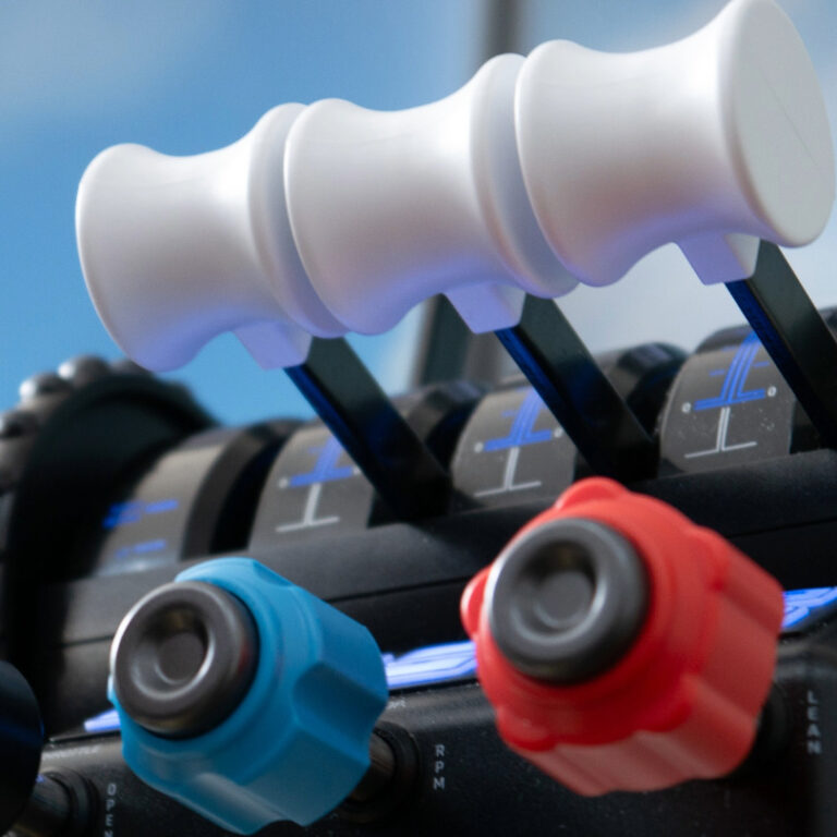 Die drei weiße Hebel mit ergonomischen Griffen des Flugsimulators, darunter zwei Knöpfe in Blau und Rot