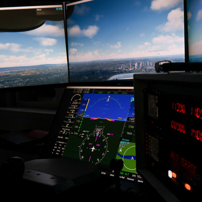 Cockpit eines Flugsimulators mit digitalen Instrumentenanzeigen und einer Panoramaansicht einer Stadt am Himmel auf mehreren Bildschirmen.